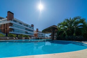 A swimming pool with a clear blue sky and a modern building in the background. - Apto vista mar 4 dormitórios e piscina (Bombinhas)
