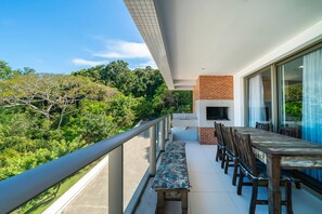A balcony with a dining table and chairs, a bench, and a view of lush greenery.