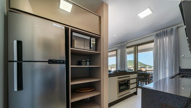 A modern kitchen with a stainless steel refrigerator, microwave, oven, and granite countertop. - Apto vista mar 4 dormitórios e piscina (Bombinhas)