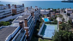 Un hotel moderno de gran altura con varias plantas, piscina en la azotea y cancha de tenis.