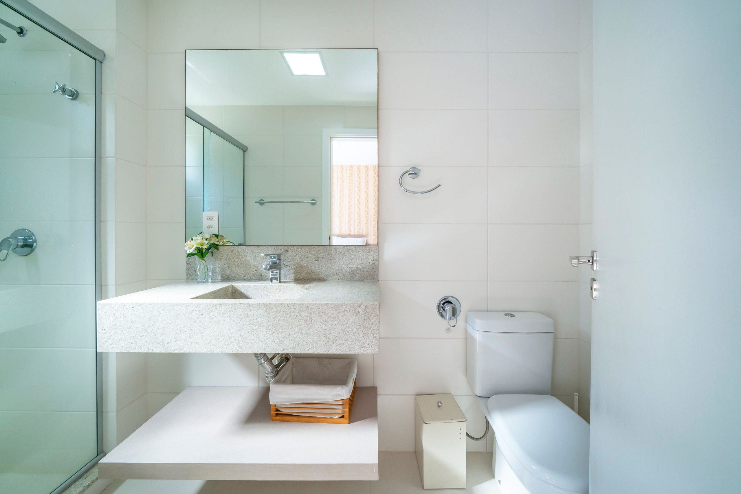 Un baño moderno con cabina de ducha de vidrio, lavabo de encimera de granito, un espejo y un inodoro.