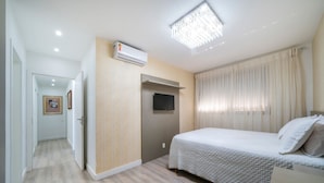 Un dormitorio con cama, televisor de pantalla plana, equipo de aire acondicionado y un pasillo que conduce a otra habitación.
