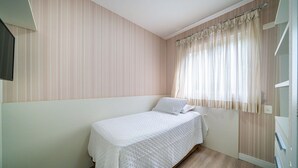 A single bed in a room with striped wallpaper, a window with sheer curtains, and a wooden floor. - Apto vista mar 4 dormitórios e piscina (Bombinhas)