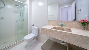 Un baño moderno con ducha envuelta en vidrio, inodoro y lavabo con encimera de mármol.