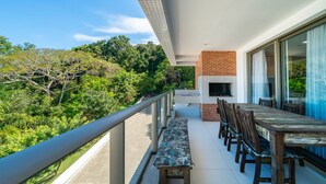 A balcony with a dining table and chairs, a bench, and a view of lush greenery. - Apto vista mar 4 dormitórios e piscina (Bombinhas)