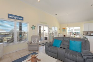 A spacious living room with a gray sectional sofa, a beige armchair, and a dining area in the background. - A SASSY SEAGULL - Super cute w/ Cargo Lift, Fenced Yard, close to beach! (Crystal Beach)