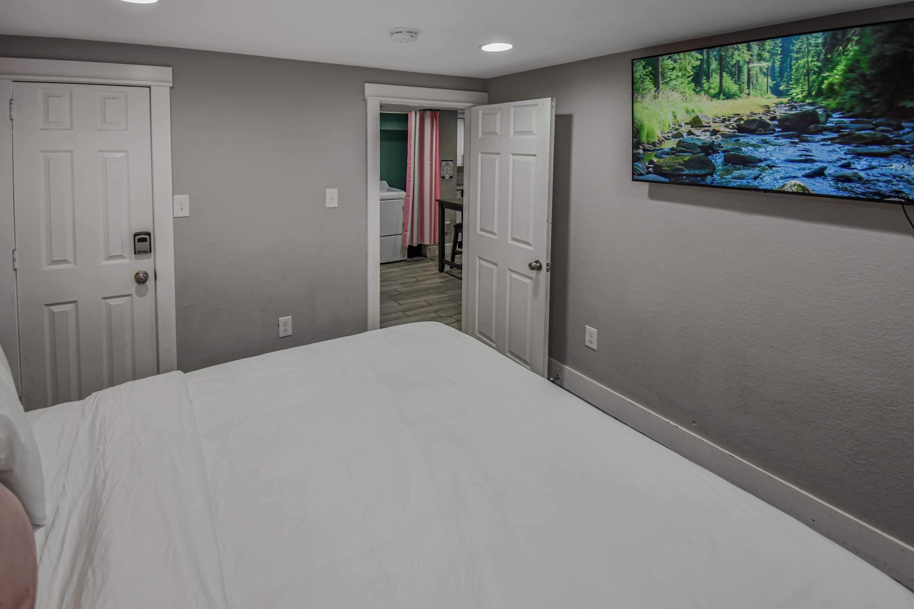 Un dormitorio con una cama, un televisor montado en la pared y una puerta que da al baño.