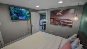 Une chambre à coucher avec un grand lit, un téléviseur fixé au mur et un tableau au-dessus du lit.