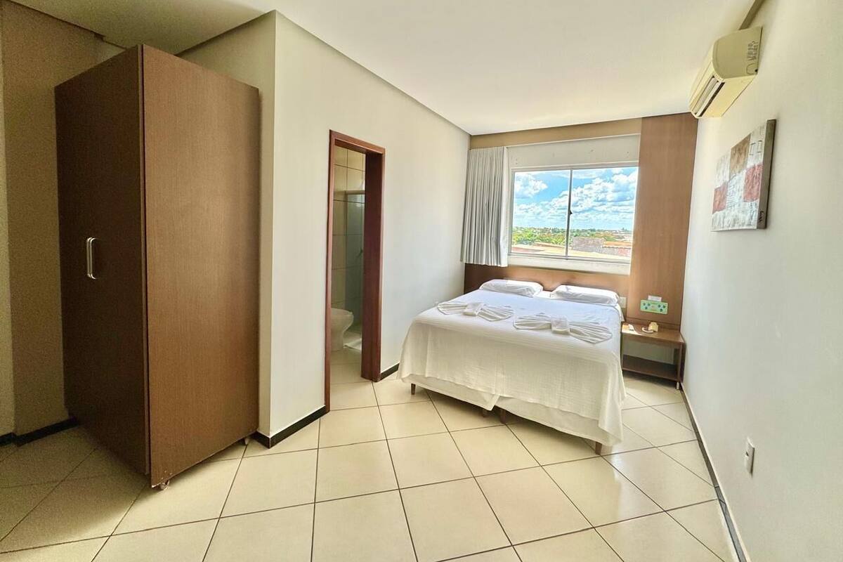 Una habitación de hotel con cama, armario, baño y ventana con vistas.