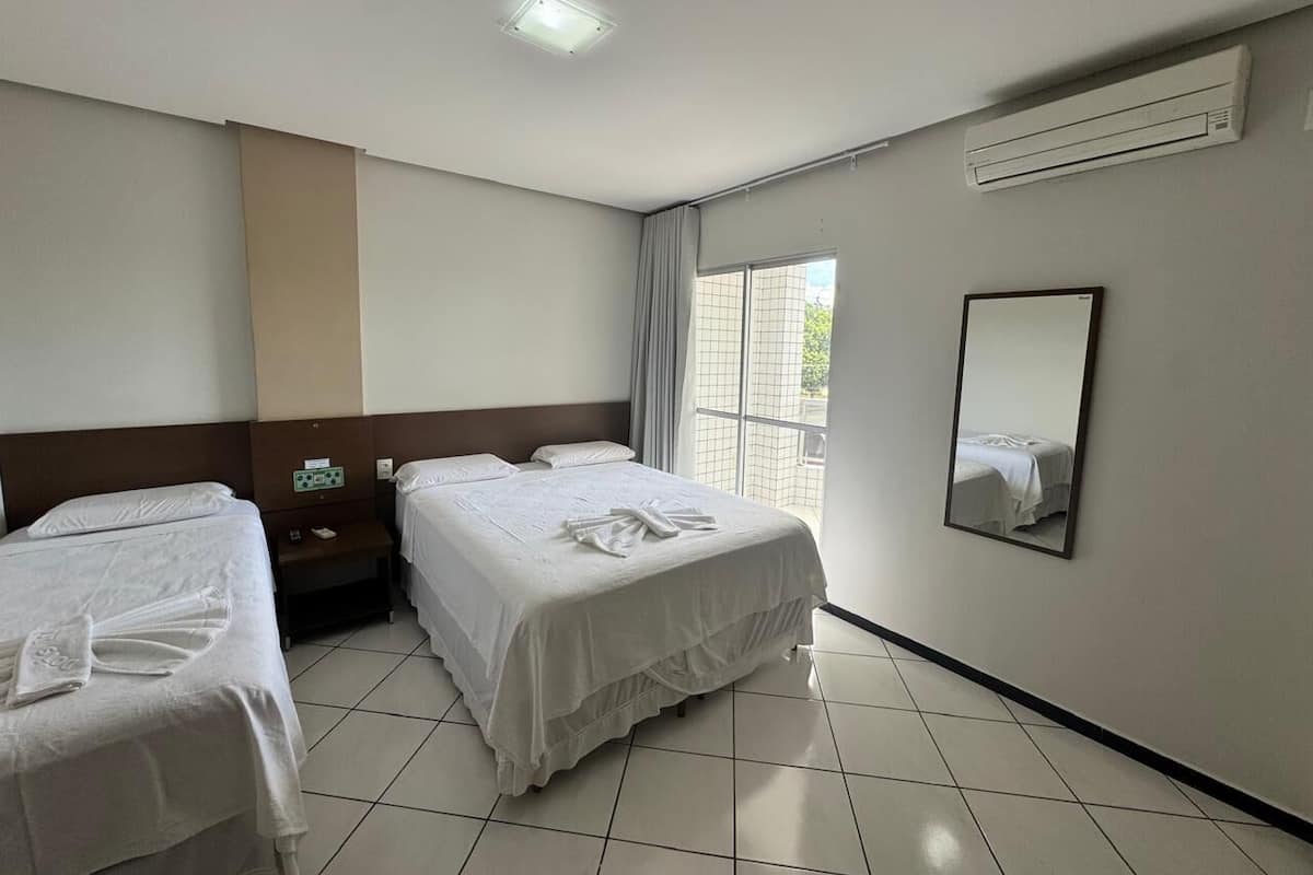 Habitación de hotel con dos camas, un ventanal grande, un equipo de aire acondicionado y un espejo en la pared.