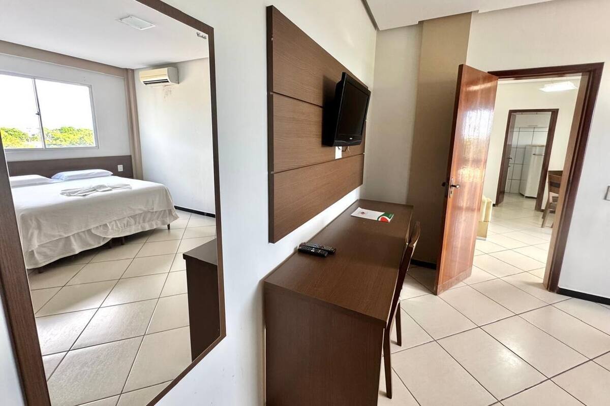 Una habitación de hotel con cama, escritorio y televisor, además de un espejo.