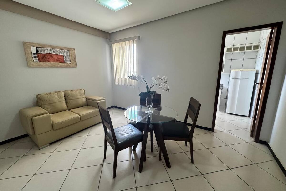 Un comedor con una mesa de vidrio, cuatro sillas, un sofá beige y una ventana con persianas.