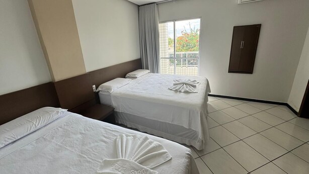 Una habitación de hotel con dos camas, una ventana con cortinas, un equipo de aire acondicionado y una puerta.