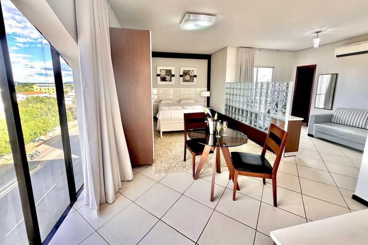 Una habitación de hotel moderna con balcón, un área de comedor con dos sillas y una mesa, una cama con cabecera y un sofá.