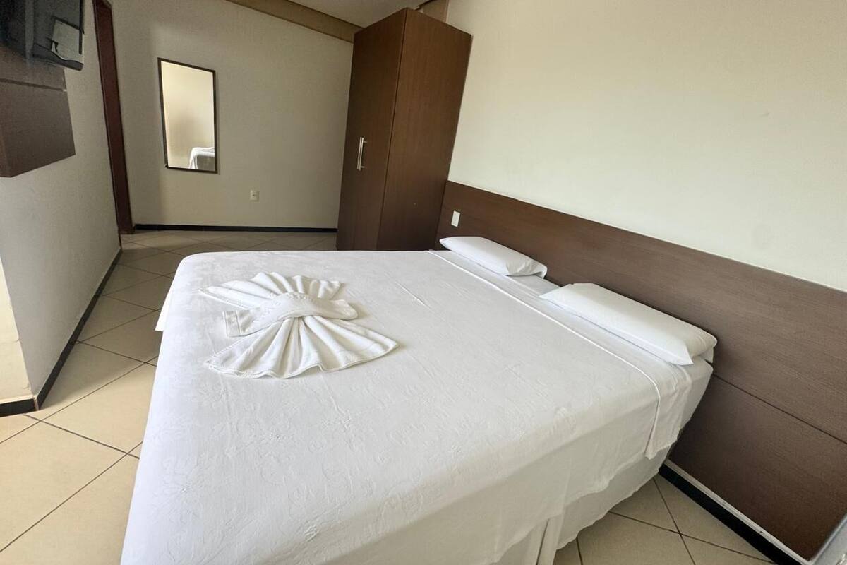 Una habitación de hotel con una cama bien hecha, un armario de madera y un espejo en la pared.