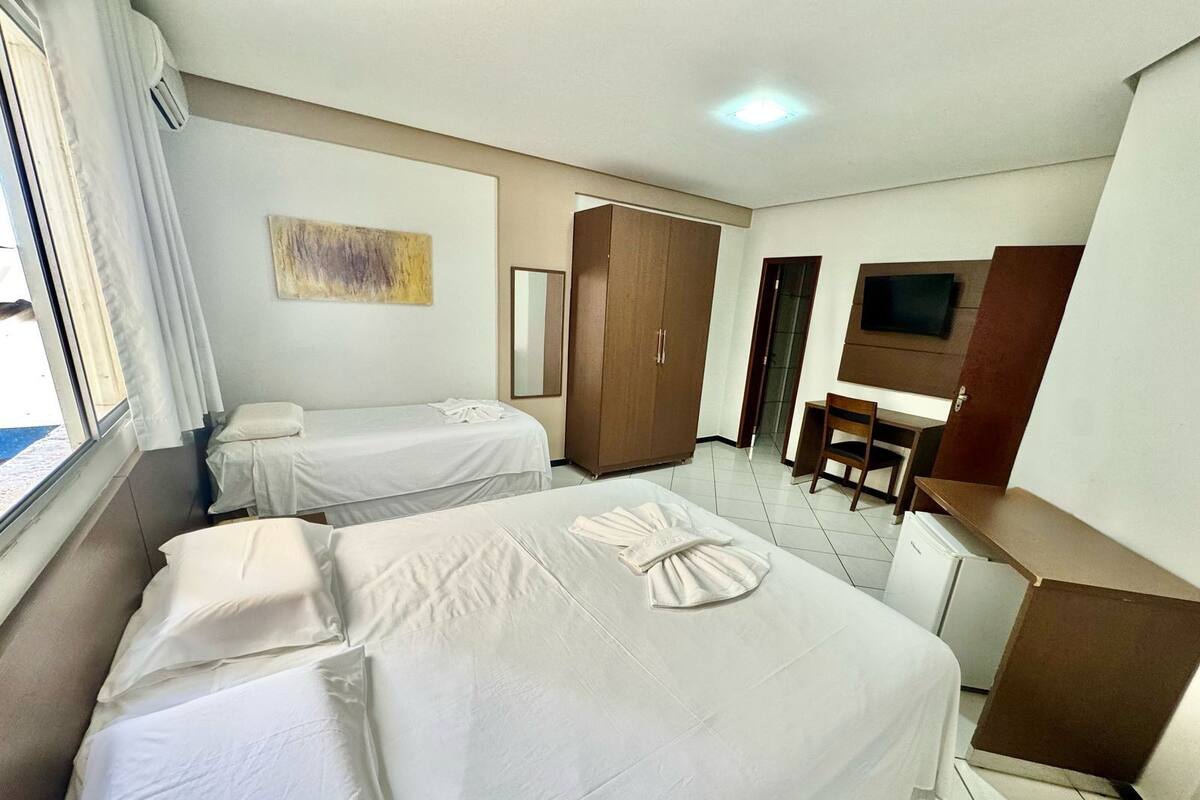 Habitación de hotel con dos camas, un escritorio, una silla, un armario y un televisor.