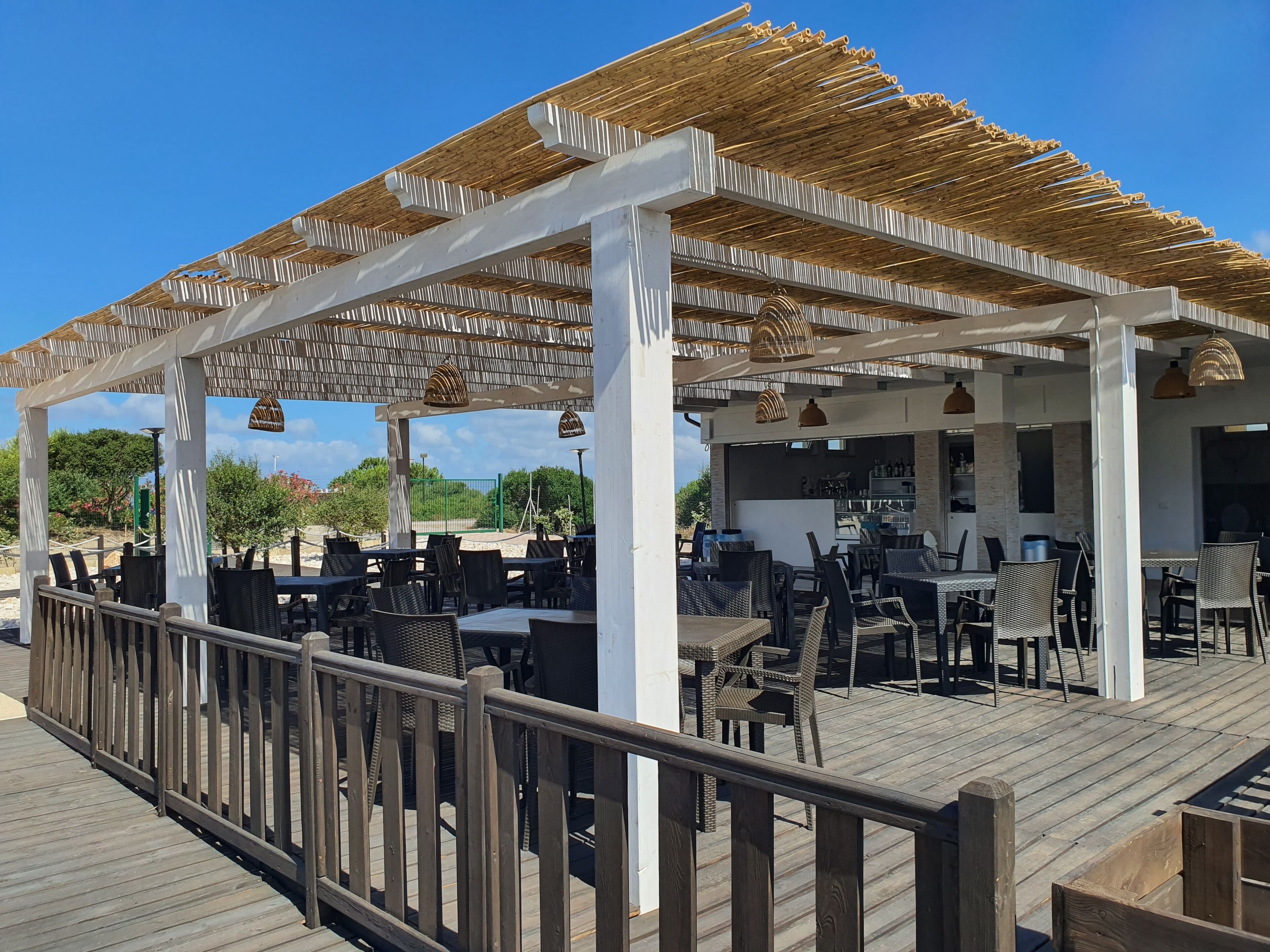 Un espace extérieur aménagé avec des tables et des chaises, une terrasse en bois et une partie couverte avec un toit de chaume.