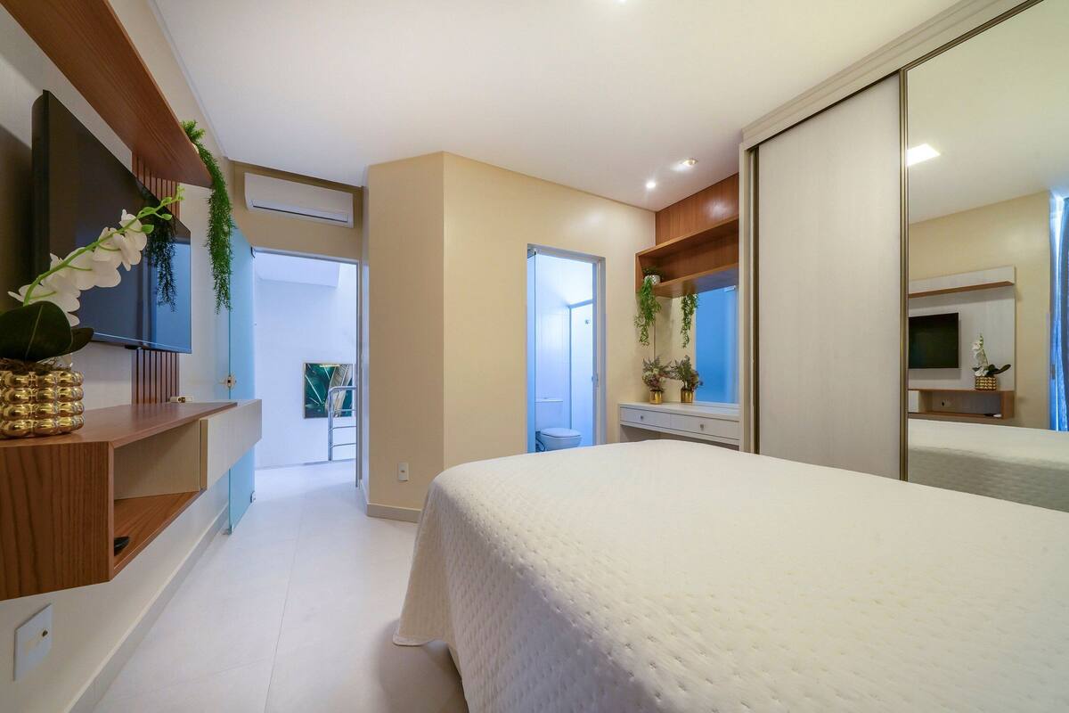 Une chambre à coucher avec un grand lit, un téléviseur fixé au mur, une console en bois et un miroir.
