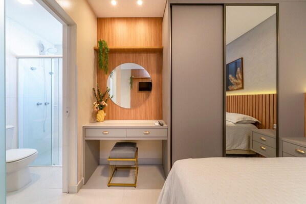 A modern bedroom with a bed, a vanity with a mirror, a small stool, and a walk-in closet. - Costão Náutico (Bombinhas)
