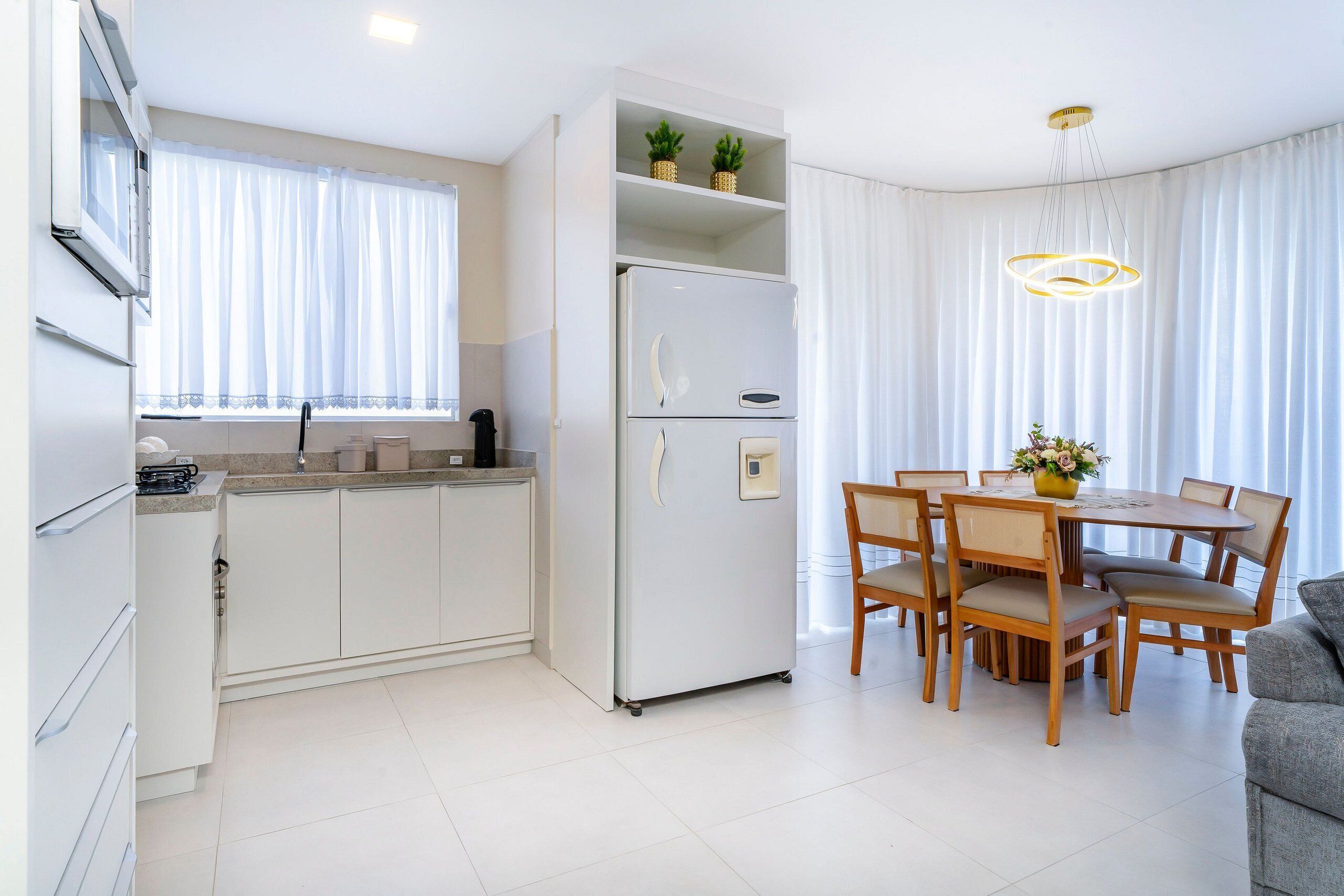 Una cucina moderna con mobili bianchi, frigorifero integrato e zona pranzo con tavolo e sedie in legno.