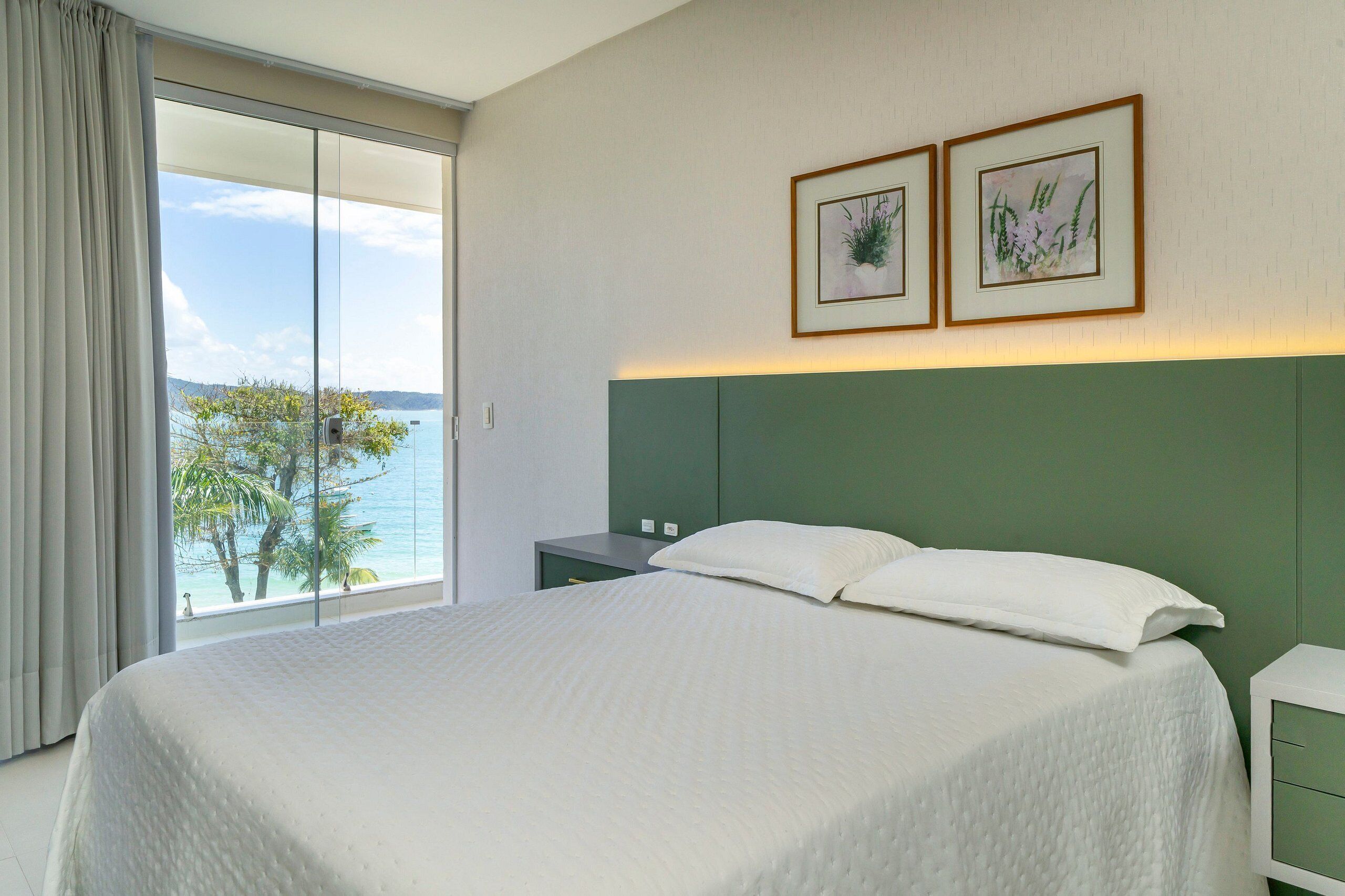Una camera da letto con un letto grande, un comodino, una testiera verde e due quadri appesi al muro.