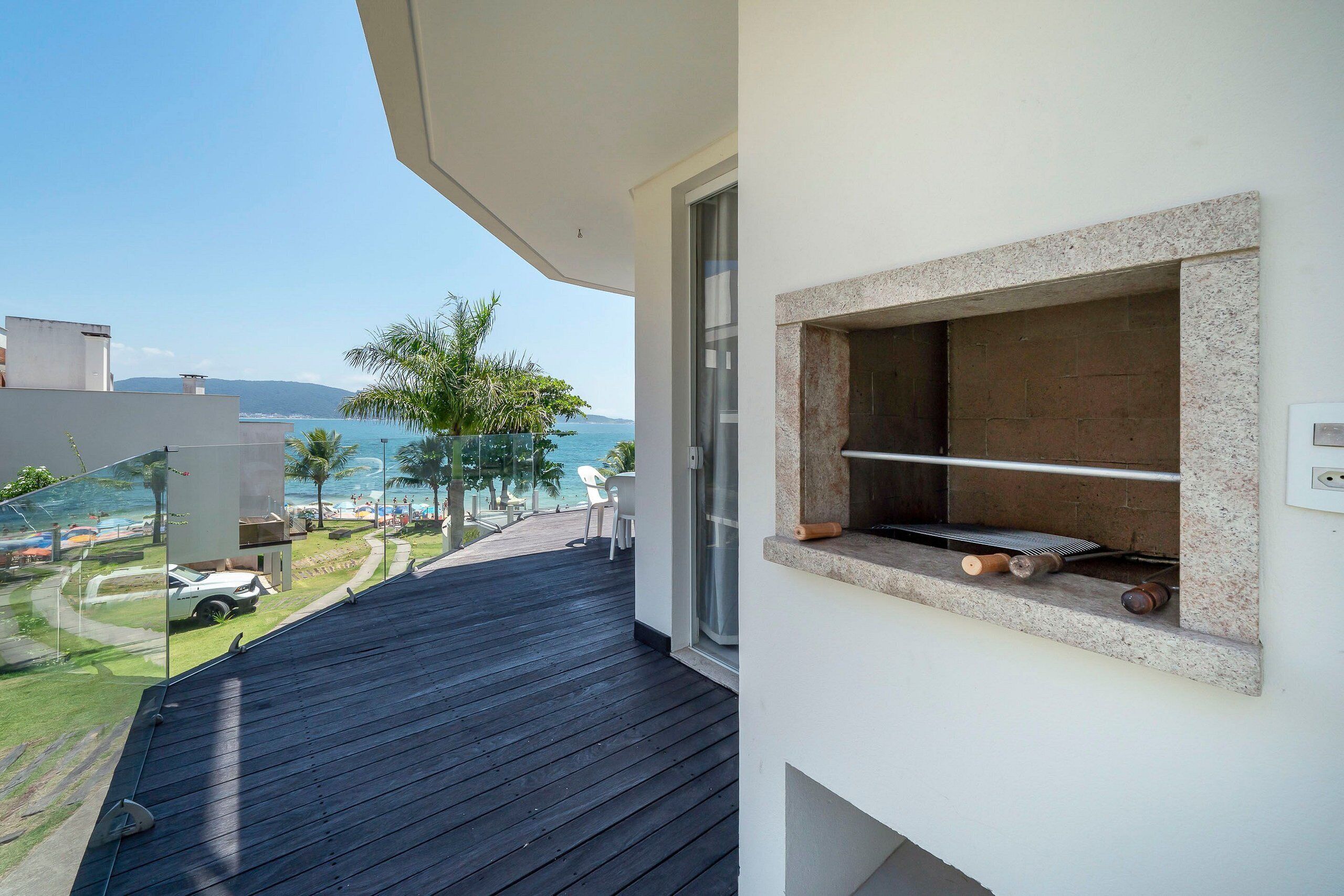 Ein Balkon mit Meerblick, einem Grill und einer Glastür, die zu einer Terrassenfläche führt.