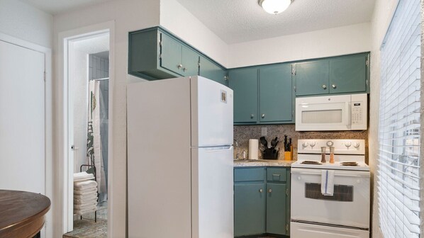 A compact kitchen with teal cabinets, a white refrigerator, a microwave, and an oven.