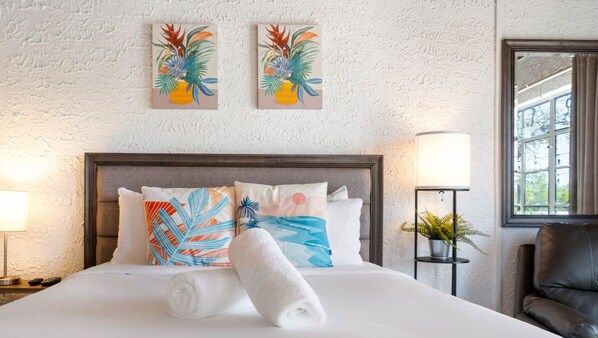 Un lit bien fait, avec une serviette enroulée, une tête de lit et deux œuvres d’art accrochées au mur.