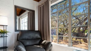 Een kamer met een leren fauteuil, een vloerlamp, een groot raam met uitzicht op bomen en een bordje met de tekst 'Bangalore #2'.