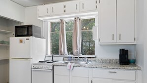 A kitchen with white cabinets, a microwave, a stove, a sink, and a window with curtains. - LakeTravis Cozy Bungalow 6 (Volente)