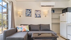 A living room with a sofa, a coffee table, and a refrigerator. There are two wall-mounted lamps and two framed pictures on the wall. - LakeTravis Cozy Bungalow 6 (Volente)