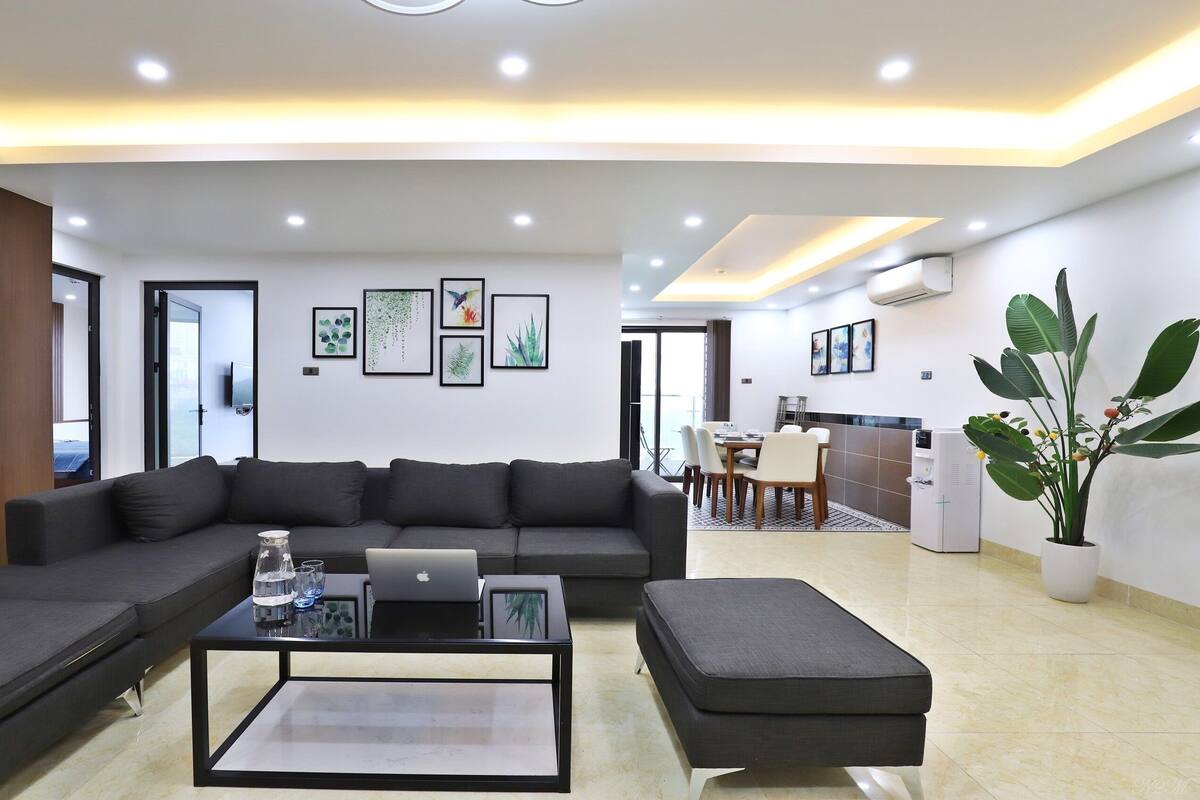 A modern living room with a sectional sofa, a coffee table with a laptop, and a dining area with chairs and a table.