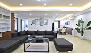 A modern living room with a sectional sofa, a coffee table with a laptop, and a dining area with chairs and a table.