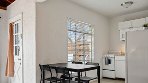 Een kleine keuken met een eettafel en stoelen, een witte koelkast en een fornuis.