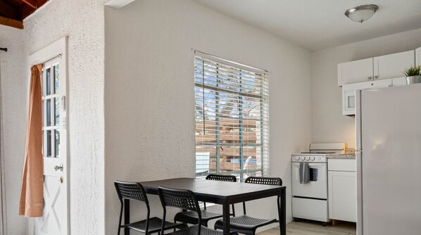A compact kitchen with a dining table and chairs, a white refrigerator, and a stove. - LakeTravis Bungalow 4 (Volente)