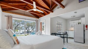 A bedroom with a large bed, a ceiling fan, and a view of the outside. There is a kitchenette with a refrigerator, stove, and microwave. - LakeTravis Bungalow 4 (Volente)