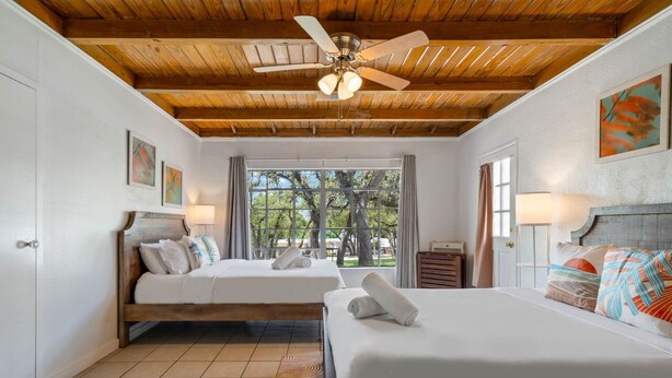 A bedroom with two beds, a ceiling fan, and a large window with a view of trees.