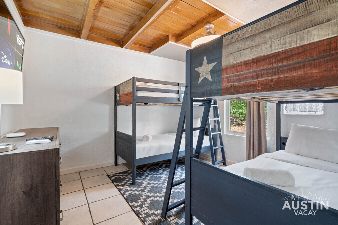Une chambre avec un lit superposé décoré de motifs d’étoiles, une échelle et un bureau avec une télécommande.