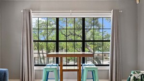 Une pièce avec une grande fenêtre, une table en bois et deux tabourets bleus.