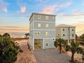 A multi-story beachfront building with a gravel driveway and palm trees.