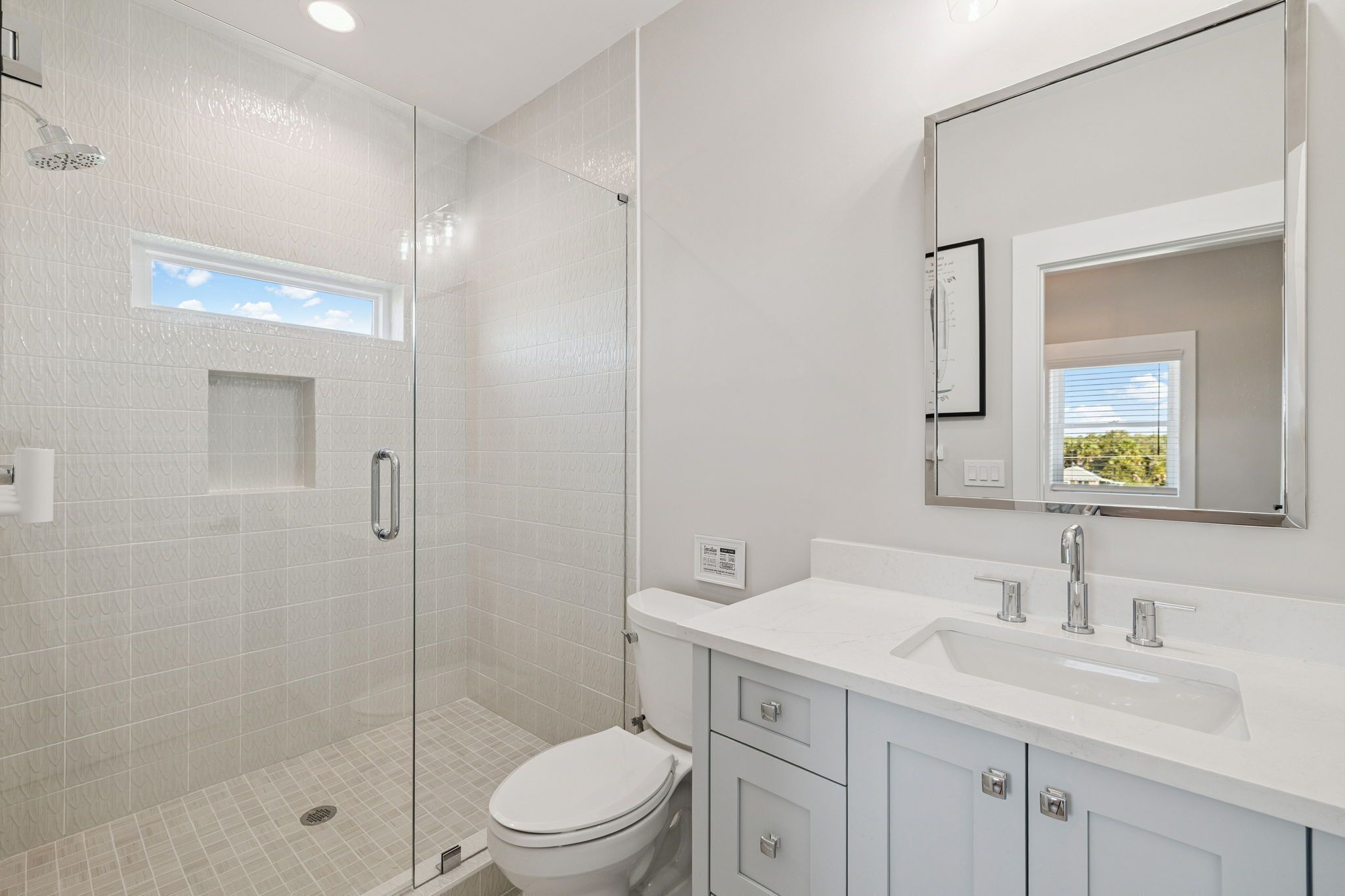 A modern bathroom with a glass-enclosed shower, a white toilet, a large mirror, and a sink with a vanity.