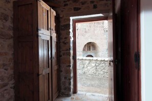 A narrow stone corridor with wooden doors and a small arched window.