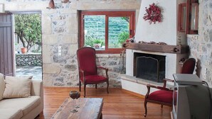 Une pièce avec un mur en pierre, une cheminée, une table en bois avec un verre à vin, un fauteuil rouge et un téléviseur.