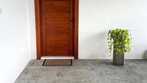 A wooden door with a metal handle, a concrete floor, and a potted plant to the right. - Meridian Holiday Resort (Ratnapura)