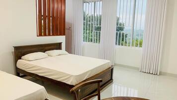 Ein Schlafzimmer mit einem hölzernen Bett, einem Sessel, einem Fenster mit Vorhängen und Blick auf grüne Vegetation.