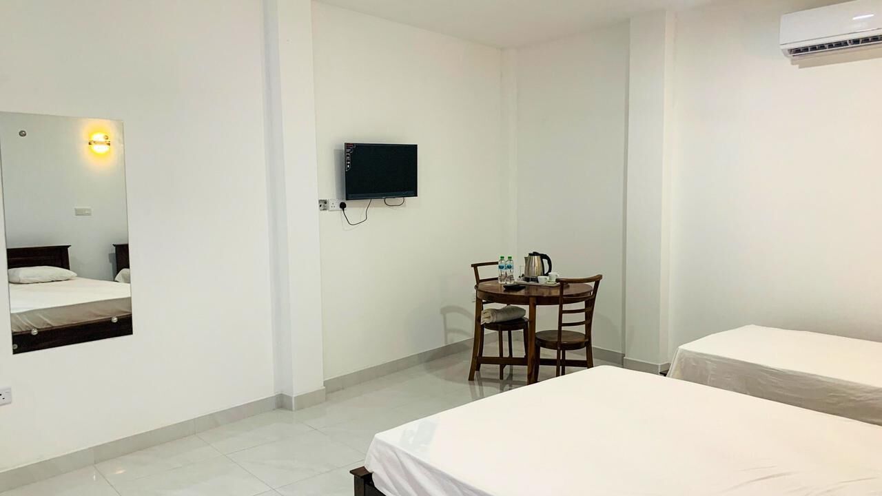A hotel room with two beds, a desk with a chair, a TV mounted on the wall, and an air conditioning unit.