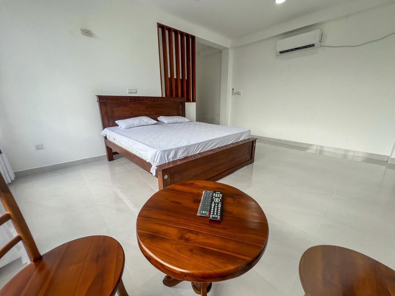 Een slaapkamer met een houten bed, een rond houten tafeltje en een stoel.
