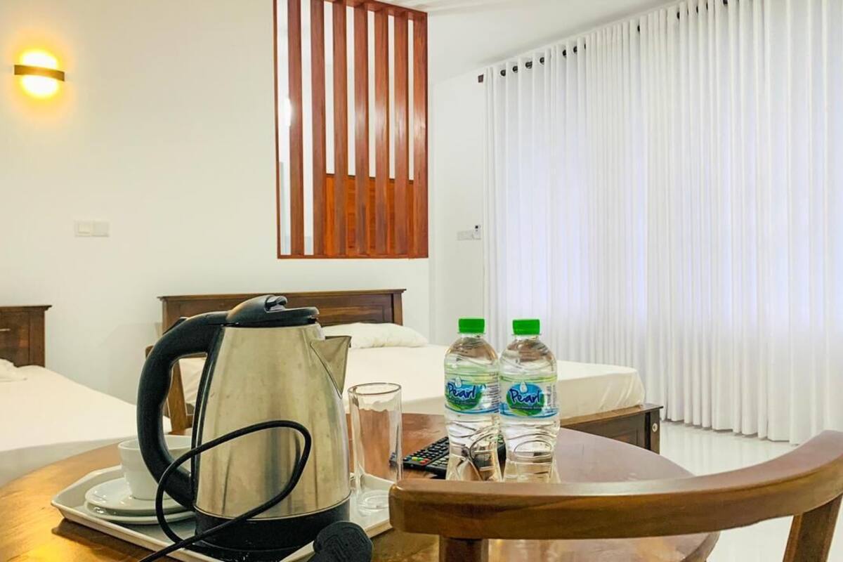 A hotel room with two beds, a kettle, two bottles of water, a tray with a cup and a glass, and a wooden chair.