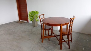 A round wooden table with four chairs, a potted plant, and a wooden door in a room with a concrete floor. - Meridian Holiday Resort (Ratnapura)