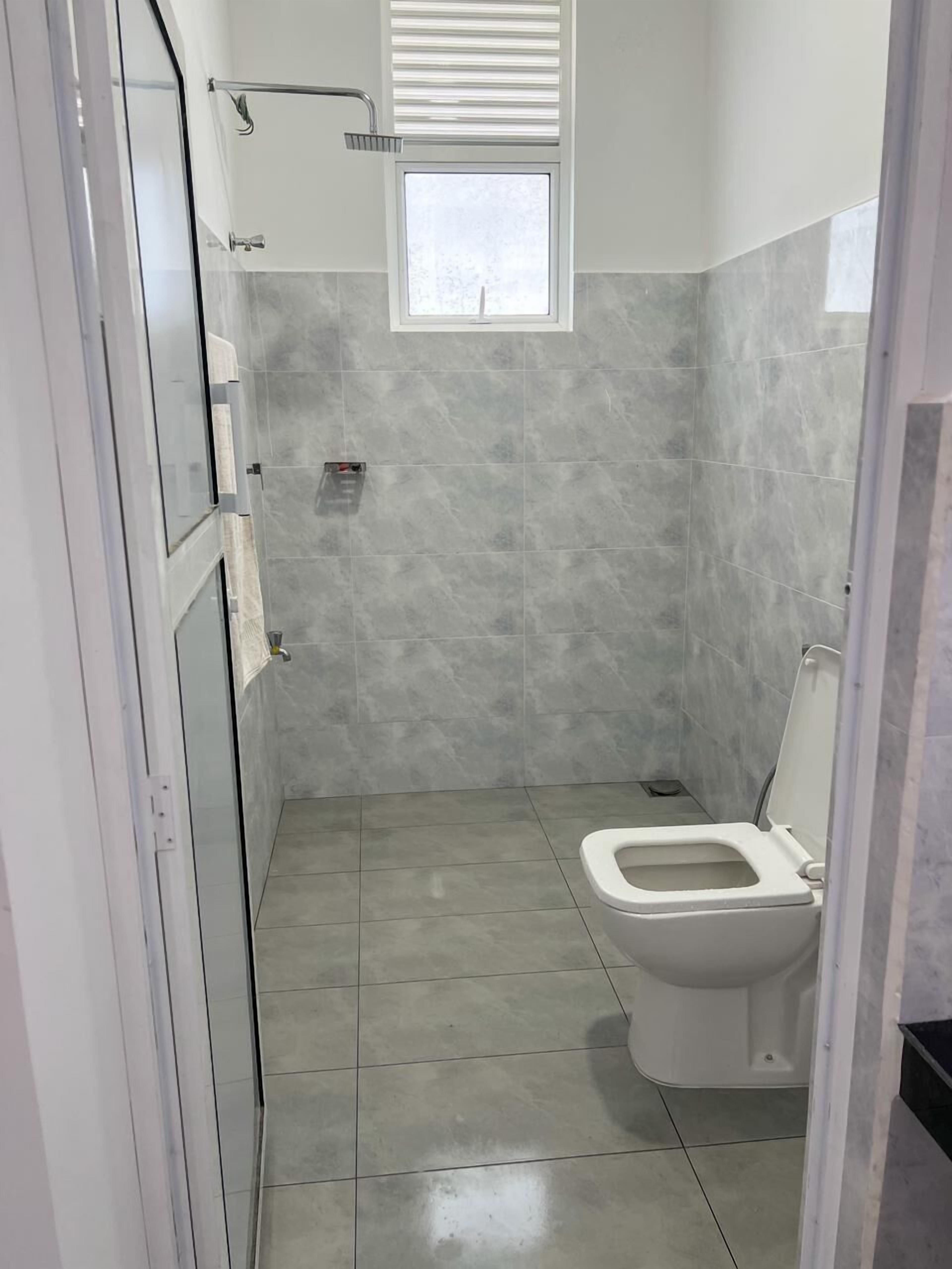 Een badkamer met een toilet, douche en raam.